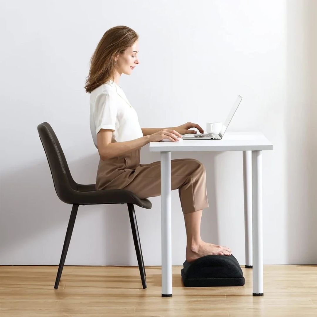 Angled ergonomic footrest placed under a desk to support both feet while seated